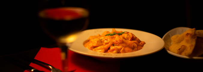 Pizzería Italiana Vittoria. Restaurante italiano en el centro de Málaga. Se ve en la foto un vino y una suculenta pasta en un ambiente muy elegante con poca luz.